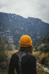 Fototapeta na wymiar Inspiring Vertical Picture of Blonde Woman with Yellow Hat Standing Looking at Nature Background From Behind