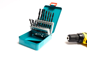 A set of drills in a metal box and an electric drill on an isolated white background.