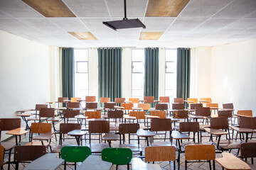 Empty classroom with desks of different colors, behind large windows for natural lighting.