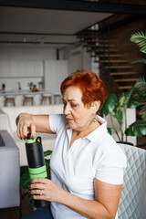 Older Caucasian woman opens sports water bottle after workout