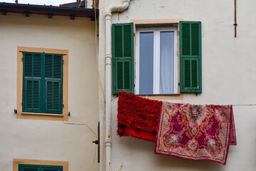 Brightly coloured carpets hang drying outside a window on the façade of an old house in the...