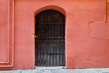 Fototapeta na wymiar Black metal arch door closed with chain and padlock on the bright pink wall of an old house in the old town of Sanremo, Imperia, Liguria, Italy