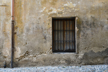 Detail of the exterior of an old house in the historic centre of Sanremo with a window closed with a metal grate and weathered wall, Imperia, Liguria, Italy