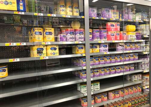 Corona, CA - Jan 26, 2022: Grocery store shelves with canisters of Enfamil and generic powdered baby formulas secured behind locked glass doors. many empty shelves due to shortages.