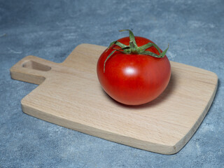 Greenhouse tomato on a small board. original size. Tomato in the kitchen.  Ripe fresh vegetable on wooden kitchen utensils.