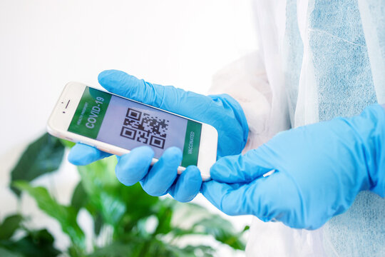 Doctor holding smartphone with Covid vaccination certificate or vaccine passport, showing proof that she is covid-19 free and has immunity for coronavirus disease . Health passport 