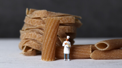 Close-up images of whole wheat pasta and miniature people. The miniature people and pasta noodles...