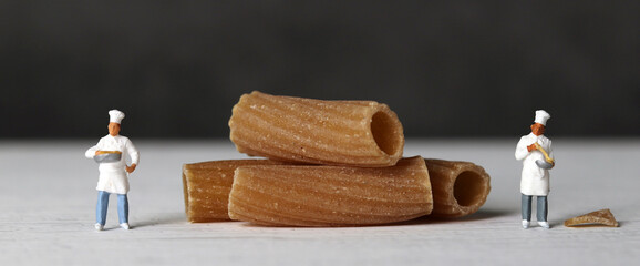 Close-up images of whole wheat pasta and two miniature chefs. The miniature people and pasta noodles with Business concept.
