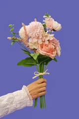 Papier Peint photo Pantone 2022 very peri Female hand holding a romantic bouquet made of pastel flowers.  Roses and other various flowers on the Very peri background. The concept of Valentine's Day or Women's Day. Spring sophisticated idea.