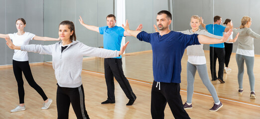 Fototapeta na wymiar Group of sporty people doing stretching exercises before dance training in modern studio