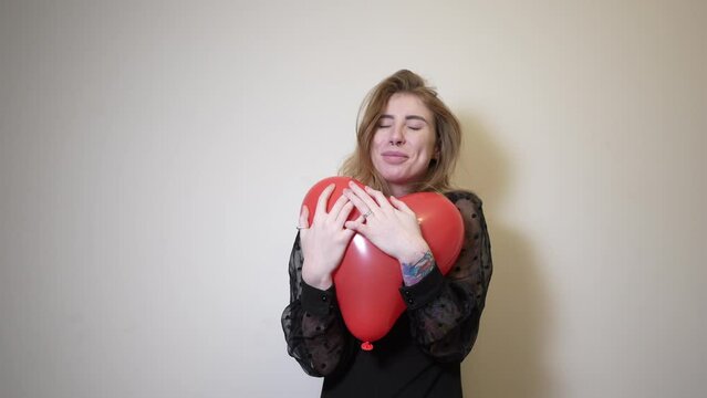 The girl holds out a heart-shaped balloon and hugs it
