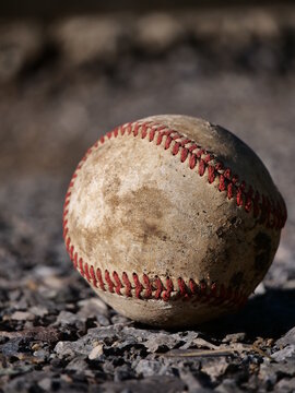 Close up, macro picture of dirty white and red baseball on gravel in the morning, afternoon, evening setting sunlight
