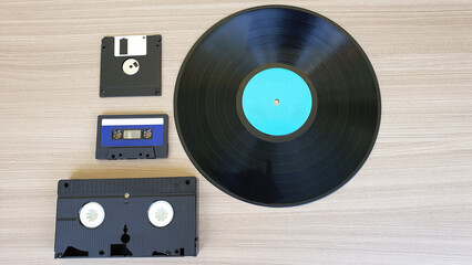Audio tape, video cassette, floppy disk and vinyl record, on a wooden background. Old technology.