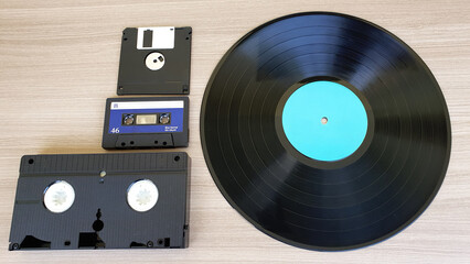 Audio tape, video cassette, floppy disk and vinyl record, on a wooden background. Old technology.