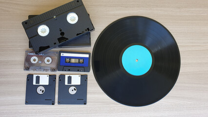 Audio tape, video cassette, floppy disk and vinyl record, on a wooden background. Old technology.