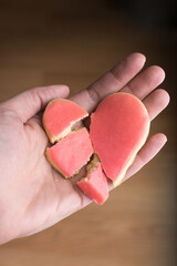 Hand holding a broken heart shaped sugar cookie; Valentine's Day heartbreak