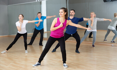 Plakat Smiling women and men of different ages warming up during dance class..