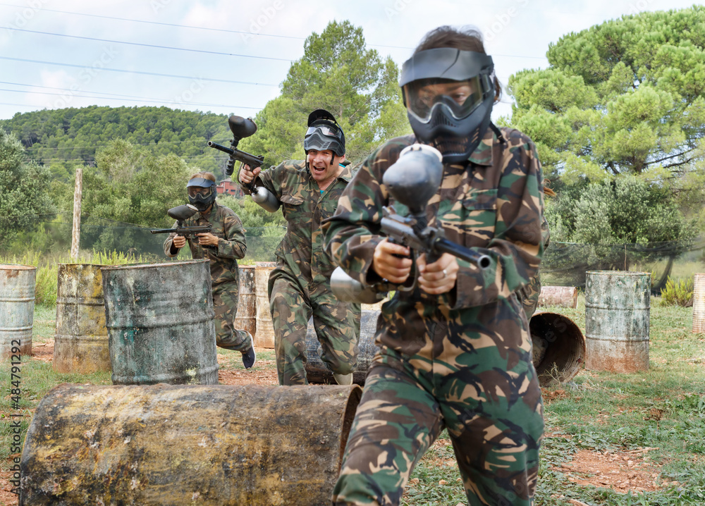 Poster Paintball players aiming and shooting with a marker guns at an opposing team outdoors