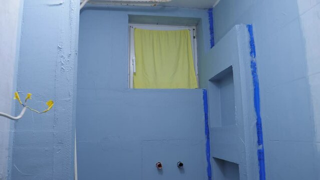 A tilt shot revealing the walls of a bathroom shower completely covered in blue waterproofing sealant, the bathroom bare after being gutted and rebuilt in a refurbishment project
