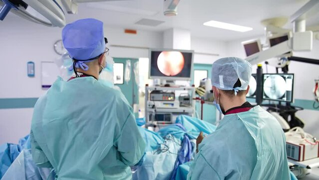 Surgery specialists operating the patient and looking at the monitor. Screen with the picture of inner organs at the backdrop in blur.
