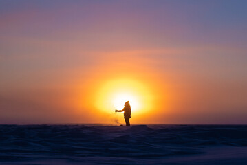 Beautiful arctic sunrise in northern Canada during peak wintertime. Woman silhouette standing in front of bright, blazing sun. 