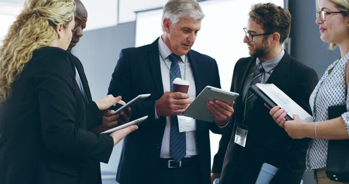 Networking is a cinch with modern tech. Diverse group of business people talking and using digital tablets together during a conference at a convention. Colleagues discussing work online