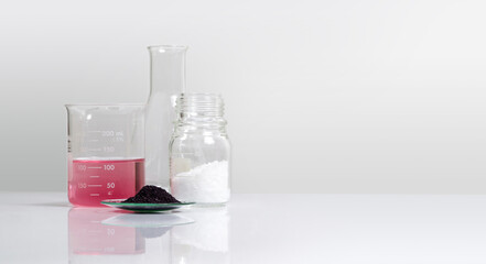 Cosmetic chemicals ingredient on white laboratory table. Potassium Permanganate Liquid in beaker, KMnO4 in chemical watch glass and Microcrystalline wax in glass container.