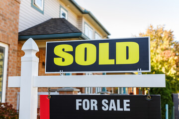 Sold yellow and black sign close-up in front of a house in a residential neighborhood
