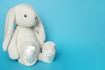 Stuffed bunny on blue background. Easter concept. Cute white toy bunny sitting on colored background.