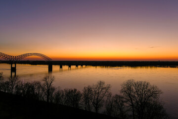 Fototapeta na wymiar a stunning aerial shot of a long metal bridge over the Mississippi river at sunset with a gorgeous blue, yellow and orange sky and lights on the bridge at Mud Island in Memphis Tennessee USA