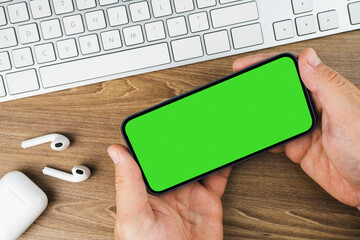 Man holding a smartphone with green screen on wooden background table. Office environment. Chroma...