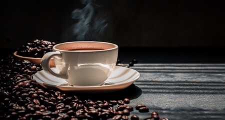 Hot coffee in a white coffee cup and many coffee beans placed around a on dark background.