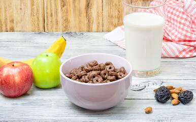 Plate with rings of chocolate cereal, Fresh fruit, a glass of milk, nuts and prunes on the slot. The concept of a healthy and fortified delicious rustic breakfast.