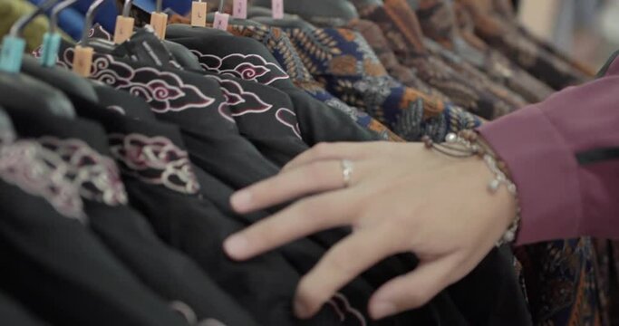Close-up shot of an unidentified Asian tourist choosing a batik shirt from a row of various batik patterns hanging in a local market. He touched the shirt with his finger. Selective Focus