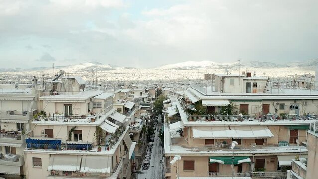 Flyover Athens cityscape winter scenery, streets full of fresh snow, snow capped mountains background