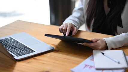 Businesswoman sitting at her office desk and checking email on digital tablet.