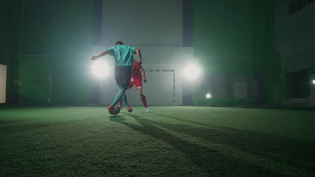 Slow motion, training day on the football club, young guys play football indoor stadium, man bypass the opponent and scores a goal, low angle view.