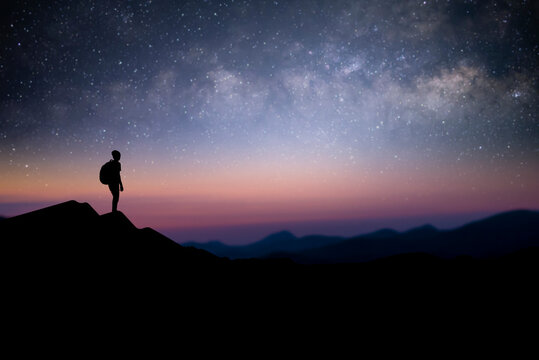 Silhouette of young male traveler with backpack standing and watching the star, milky way over the sky alone on top of the mountain. He enjoyed traveling and was successful when he reached the summit.