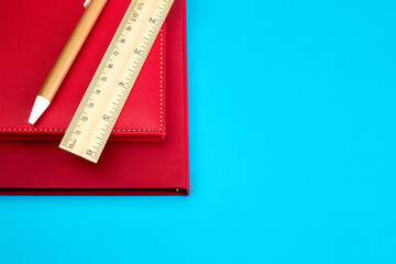 Vivid red notebook, beige stationery - ruler, pen, eraser and pencil sharpener on vivid sky blue background, simple and minimalistic