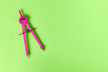 Bright pink compass, geometry or architecture tool, against vivid green background