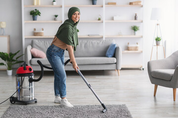Cheerful muslim woman cleaning rug carpet with vacuum cleaner
