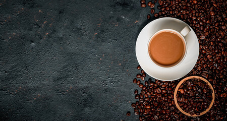 Hot coffee in a white coffee cup and many coffee beans placed around a on dark background.