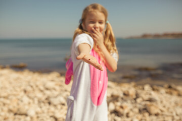 A pretty girl holds a ladybug in her palm. Child dressed in unicorn kigurumi walking on the seashore
