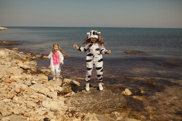 Two pretty girls in kigurumi cow and unicorn walk on the seashore, friends chat and play