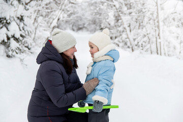 Mother and little daughter in the winter park, forest look at each other and enjoy communication.