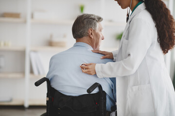 Fototapeta premium Female doctor using stethoscope on older man in wheelchair at home