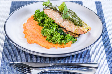 A seafood dinner serving of a piece of Atlantic Salmon on top of sweet potato mash and kale.
