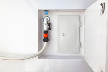A water tap with a hose connected to it on the hull of the yacht. A place for water supply on a yacht.
