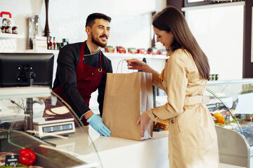 Shop assistant handling shopping bag to female customer in grocery store