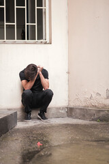 Young man sitting in the corner alone with his hands over his face, agonizing over his problem